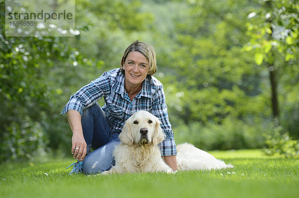 Reife Frau mit einem Golden Retriever im Garten