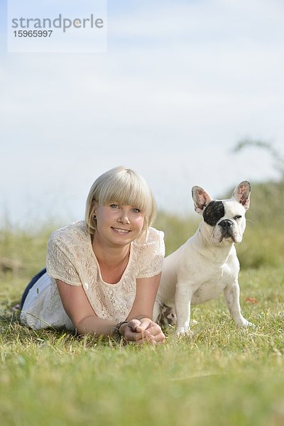 Frau liegt auf einer Wiese mit einer sieben Monate alten Französischen Bulldogge