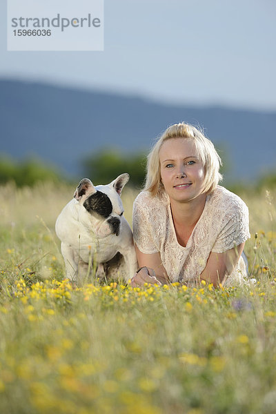 Frau liegt auf einer Wiese mit einer sieben Monate alten Französischen Bulldogge