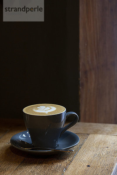 Nahaufnahme einer Tasse Cappuccino auf einem rustikalen Holztisch in einem Cafe.