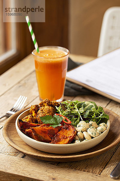 Nahaufnahme eines Glases mit Karottensaft und einer Schüssel mit gemischtem Gemüse in einem Cafe.