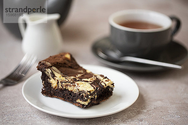 Nahaufnahme einer Tasse Tee und eines Schokoladenkäsekuchens auf weißem Teller in einem Cafe.