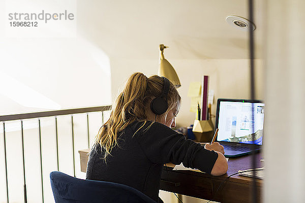 Teenagerin mit Kopfhörern  die zu Hause auf einen Laptop-Computer schaut