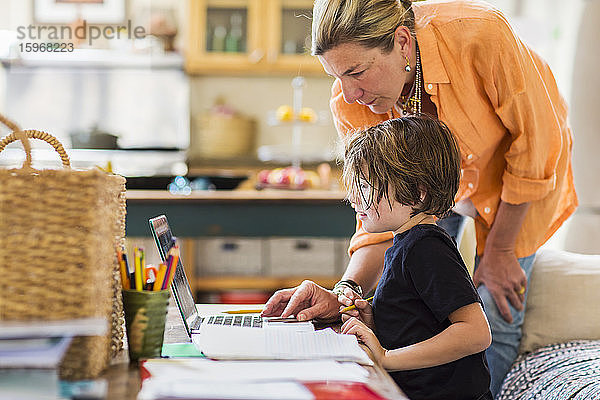 Eine erwachsene Frau hilft ihrem sechsjährigen Sohn bei einer Fernlernsitzung auf einem Laptop mit einem Touchpad.