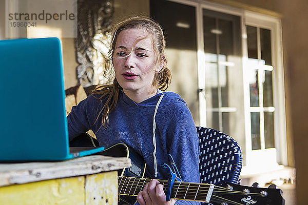 Ein junges Mädchen  das sich einen Laptop anschaut  singt und Gitarre spielt