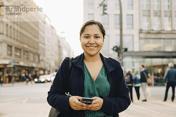 Porträt einer lächelnden Unternehmerin mit stehendem Telefon in der Stadt