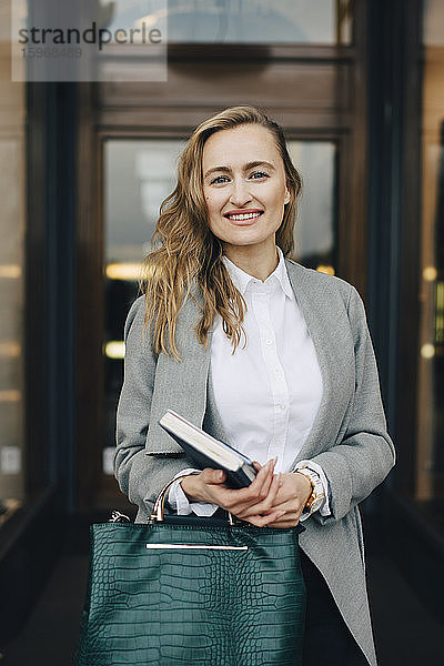 Porträt einer lächelnden Geschäftsfrau mit Buch und Tasche in einem Geschäft in der Stadt