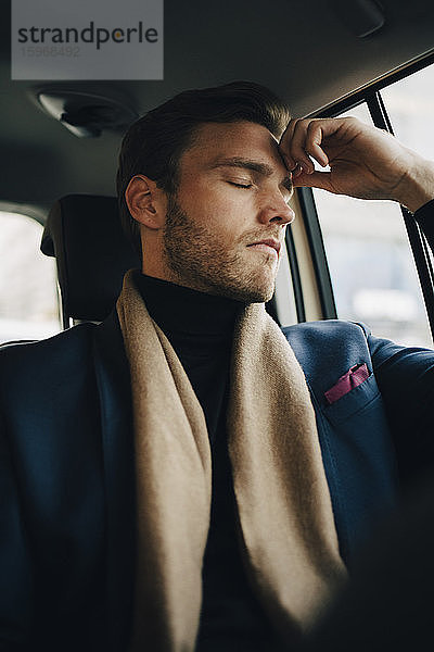 Trauriger Geschäftsmann im Anzug mit geschlossenen Augen im Taxi sitzend