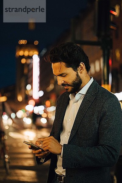 Mann benutzt Smartphone  während er nachts in der Stadt steht