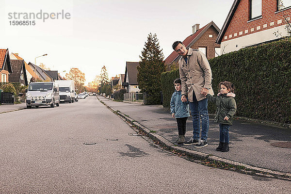 Vater steht im Herbst mit Kindern auf dem Bürgersteig