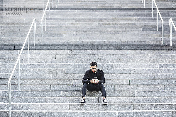 Junger Mann benutzt Smartphone  während er auf einer Treppe sitzt