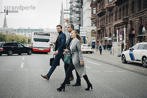 Geschäftsfrau mit männlichen Kollegen überqueren Straße in der Stadt