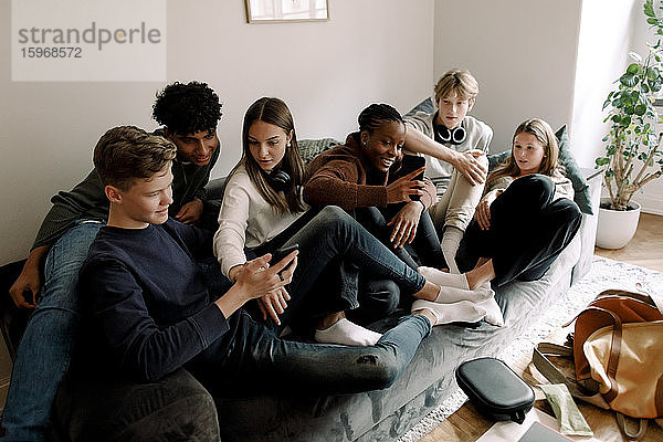 Männliche und weibliche Freunde im Teenageralter benutzen Mobiltelefone  während sie zu Hause auf dem Sofa sitzen