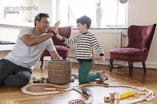 Lächelnder Vater gibt dem Sohn High-Five  während er mit Spielzeug im Wohnzimmer sitzt