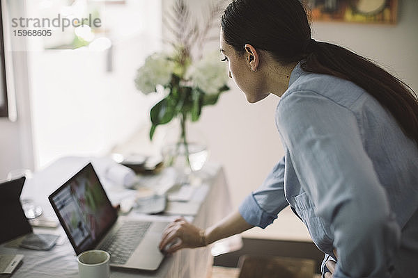 Seitenansicht einer Unternehmerin mit einem Laptop auf einem Tisch im Heimbüro