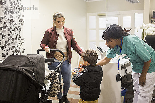 Kinderarzt gibt Aufkleber an Junge  während Mutter mit Kinderwagen im Krankenhaus steht