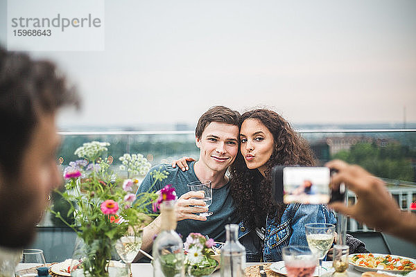 Geschnittene Hand eines Mannes  der während der Party ein Foto des Paares durch das Telefon auf der Terrasse anklickt