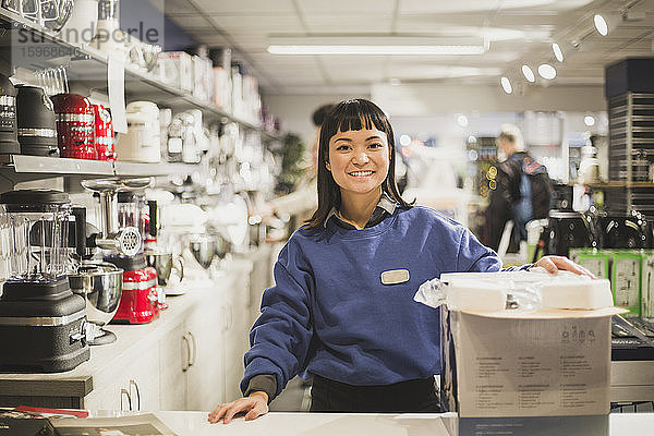 Porträt einer lächelnden Verkäuferin mit im Laden stehendem Gerät