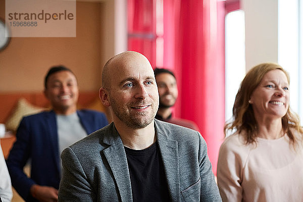 Lächelnder männlicher Unternehmer sitzt mit Kollegen in Bürobesprechung am Arbeitsplatz