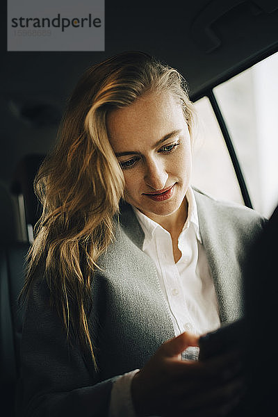 Geschäftsfrau nutzt Internet über Smartphone  während sie während einer Geschäftsreise im Taxi sitzt