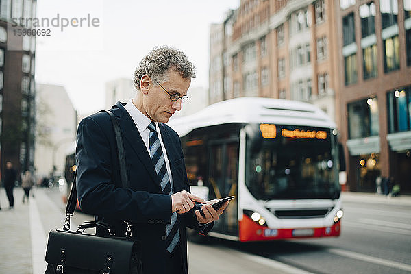 Ein reifer Geschäftsmann benutzt ein Smartphone  während er in der Stadt steht