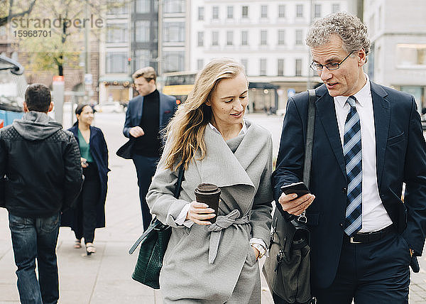 Geschäftsmann zeigt einer Mitarbeiterin ein Smartphone beim Spaziergang in der Stadt
