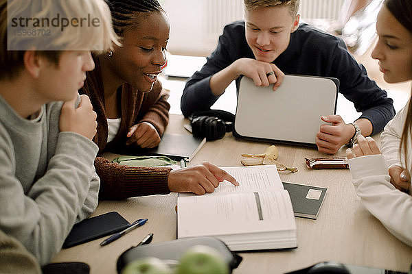 Teenagerin liest Lehrbuch  während sie mit Freunden zu Hause studiert