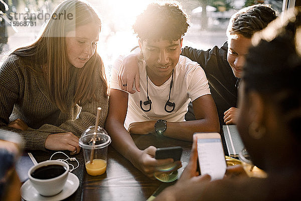 Mädchen und Jungen im Teenageralter surfen mit Mobiltelefonen im Internet  während sie im Café sitzen