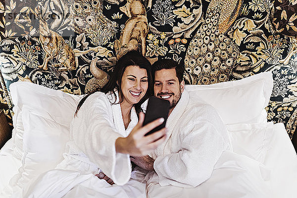 Glückliche Frau und Mann im mittleren Erwachsenenalter  die sich im Hotelzimmer im Bett betten