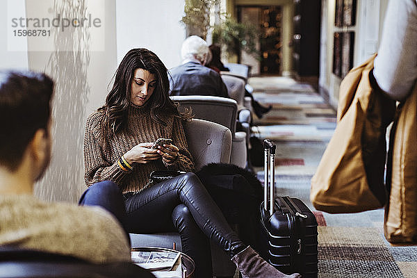Mittlere erwachsene Frau  die ein Mobiltelefon benutzt  während sie im Hotel vor ihrem Freund sitzt