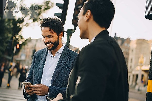 Lächelnder Mann benutzt Telefon  während er einem männlichen Freund in der Stadt zur Seite steht