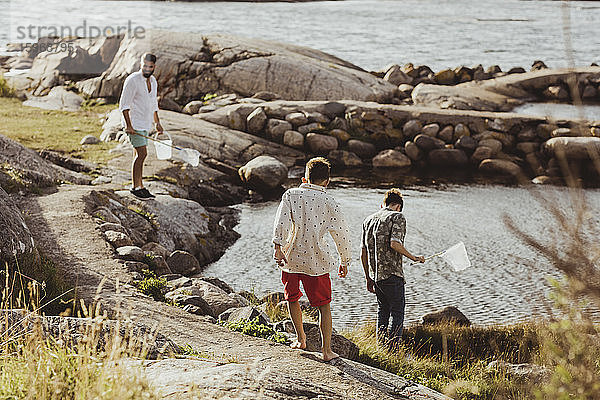 Rückansicht eines Jungen mit Geschwisterkind  während der Vater am Wochenende über einem Felsen steht