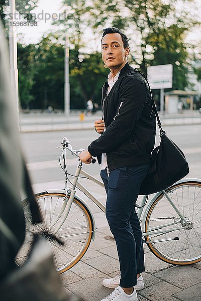 Junger Mann schaut weg  während er in der Stadt ein Fahrrad hält