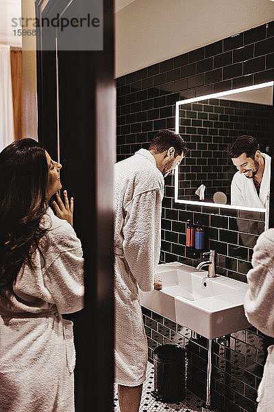 Lächelnde Frau sieht Mann an  der im Badezimmer vor dem Spiegel steht