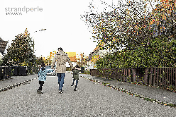 Rückansicht eines Vaters  der im Herbst mit Kindern auf einem Fußweg geht
