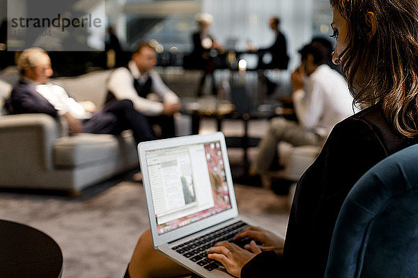 Geschäftsfrau benutzt Laptop mit Kollegen  die im Hintergrund im Büro sitzen