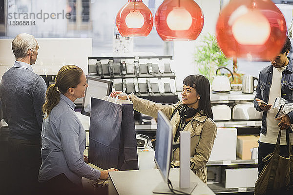 Lächelnder Kunde hält Einkaufstasche in der Hand  während er im Elektronikladen mit dem reifen Besitzer spricht