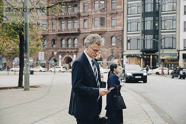Seitenansicht eines reifen Geschäftsmannes  der ein Smartphone benutzt  während er in der Stadt steht