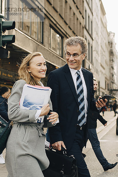 Lächelnde Unternehmerin mit männlichem Kollegen überquert Straße in der Stadt