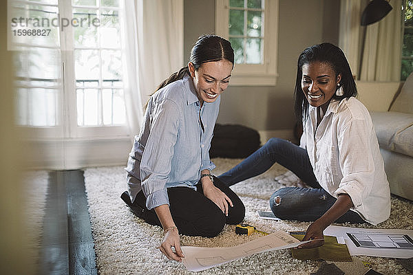 Lächelnde Designerinnen diskutieren  während sie im Heimbüro auf dem Teppich sitzen