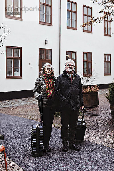 Porträt eines älteren Ehepaares  das mit Gepäck auf einem Fußweg vor einem Hotel steht