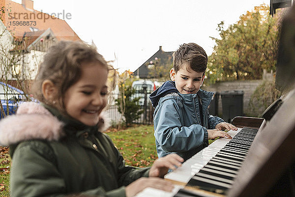 Lächelndes Mädchen spielt Klavier mit Bruder im Hinterhof