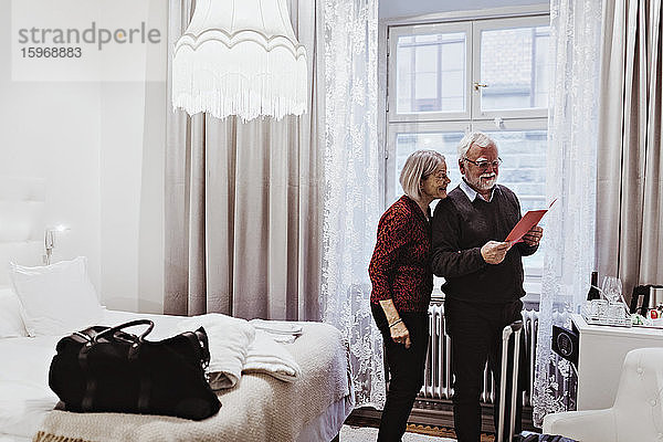 Lächelndes älteres Ehepaar liest Karte  während es im Hotelzimmer steht