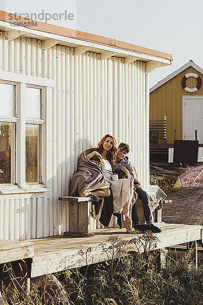 Porträt einer lächelnden Mutter und eines lächelnden Sohnes  die sich an einem sonnigen Tag an die Kabine setzen