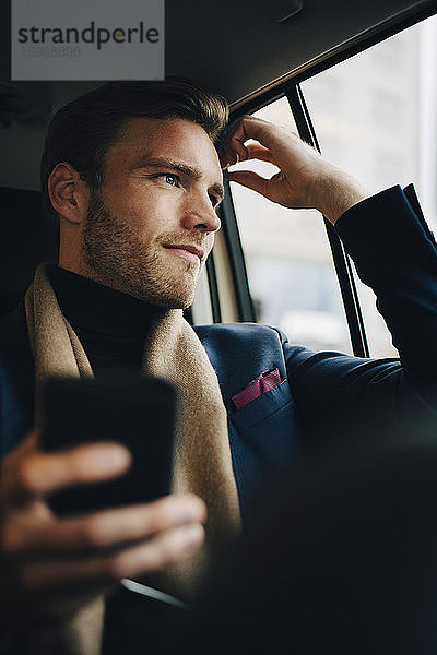Selbstbewusster Geschäftsmann im Anzug  der im Taxi sitzend durchs Fenster schaut