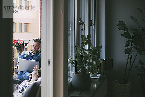 Mann arbeitet am Laptop und entspannt sich auf dem Balkon