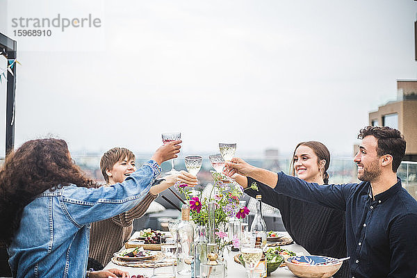 Männliche und weibliche Freunde stoßen Wein an  während sie zum Abendessen auf der Terrasse sitzen