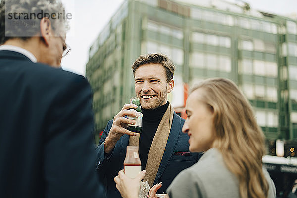 Lächelnder männlicher Unternehmer mit einem Getränk  der Mitarbeiter in der Stadt ansieht