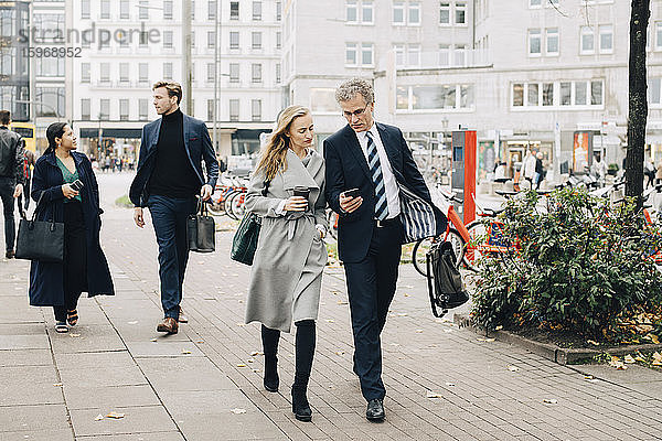 Geschäftsmann zeigt einer Kollegin ein Smartphone beim Spaziergang in der Stadt