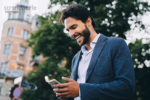 Fröhlicher Mann benutzt Smartphone  während er in der Stadt steht